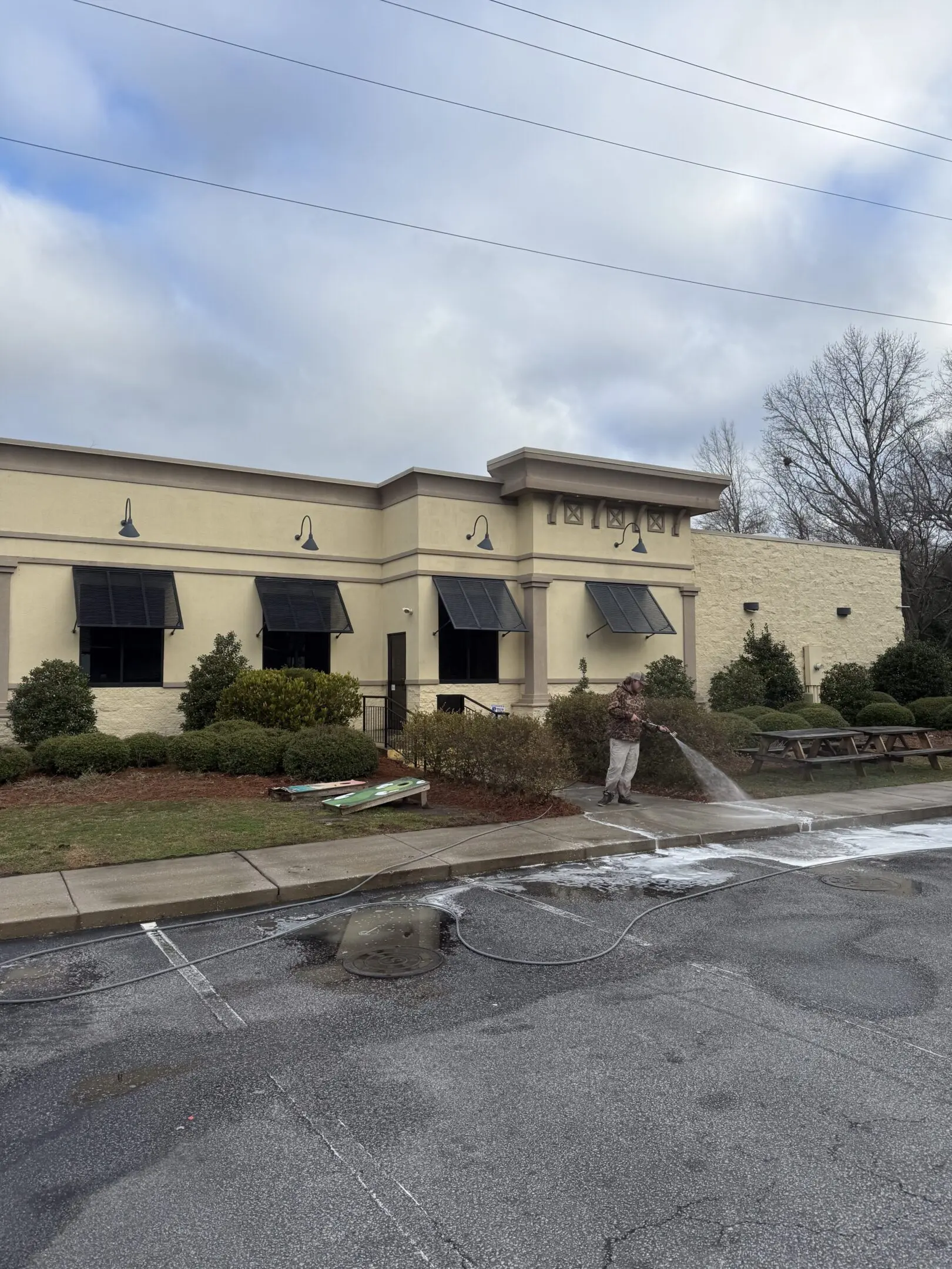 Exterior view of a beige restaurant with outdoor seating and a parking lot.