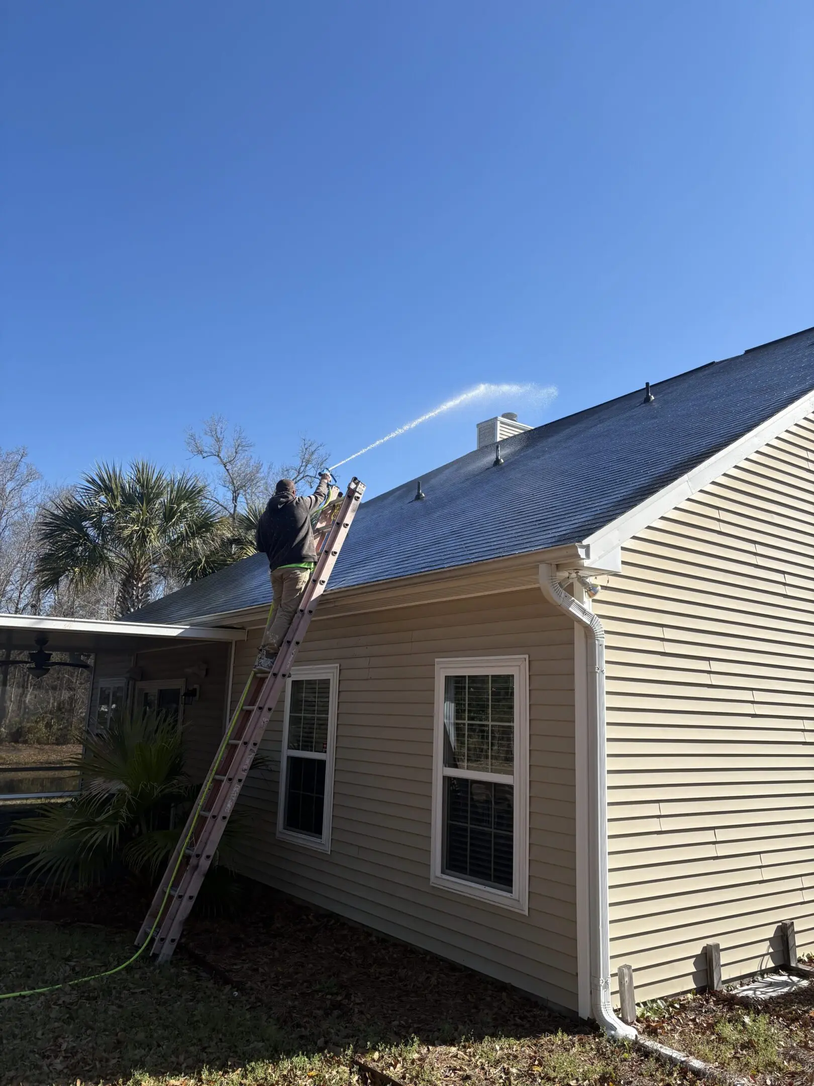 Man working on a roof under clear blue sky.