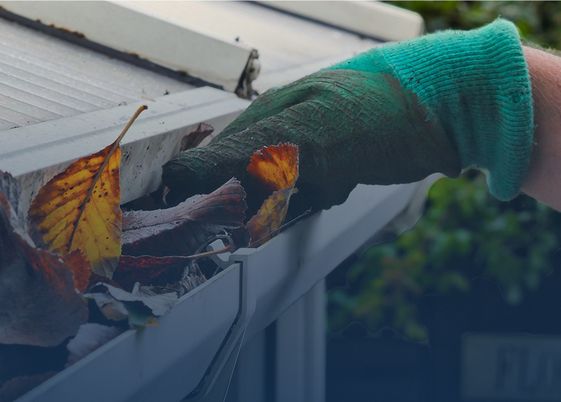 Gloved hand cleaning leaves from gutter.