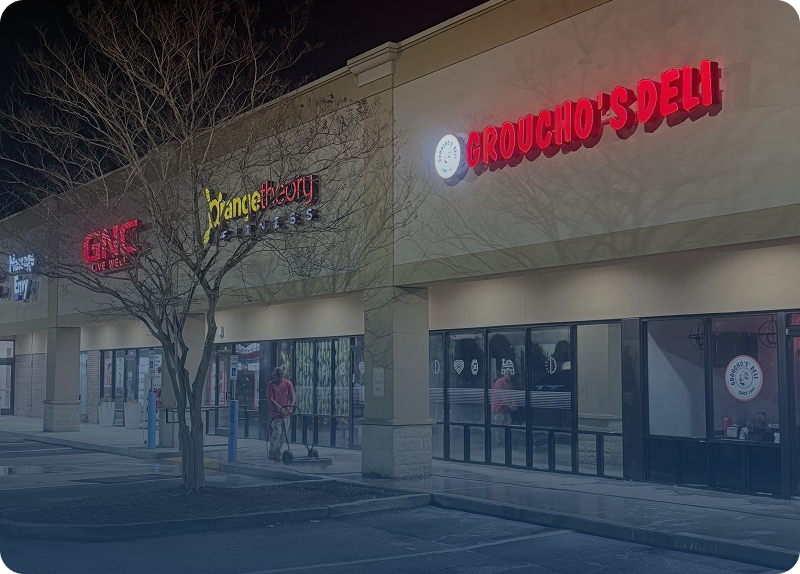 Exterior of two adjacent stores, Juice Bar and Trougho's Deli, at night.
