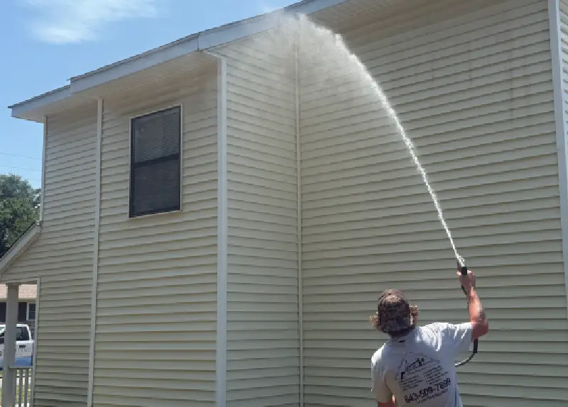 Person power washing the side of a house on a sunny day.