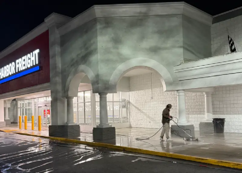 Person power washing the exterior of a commercial building at night.